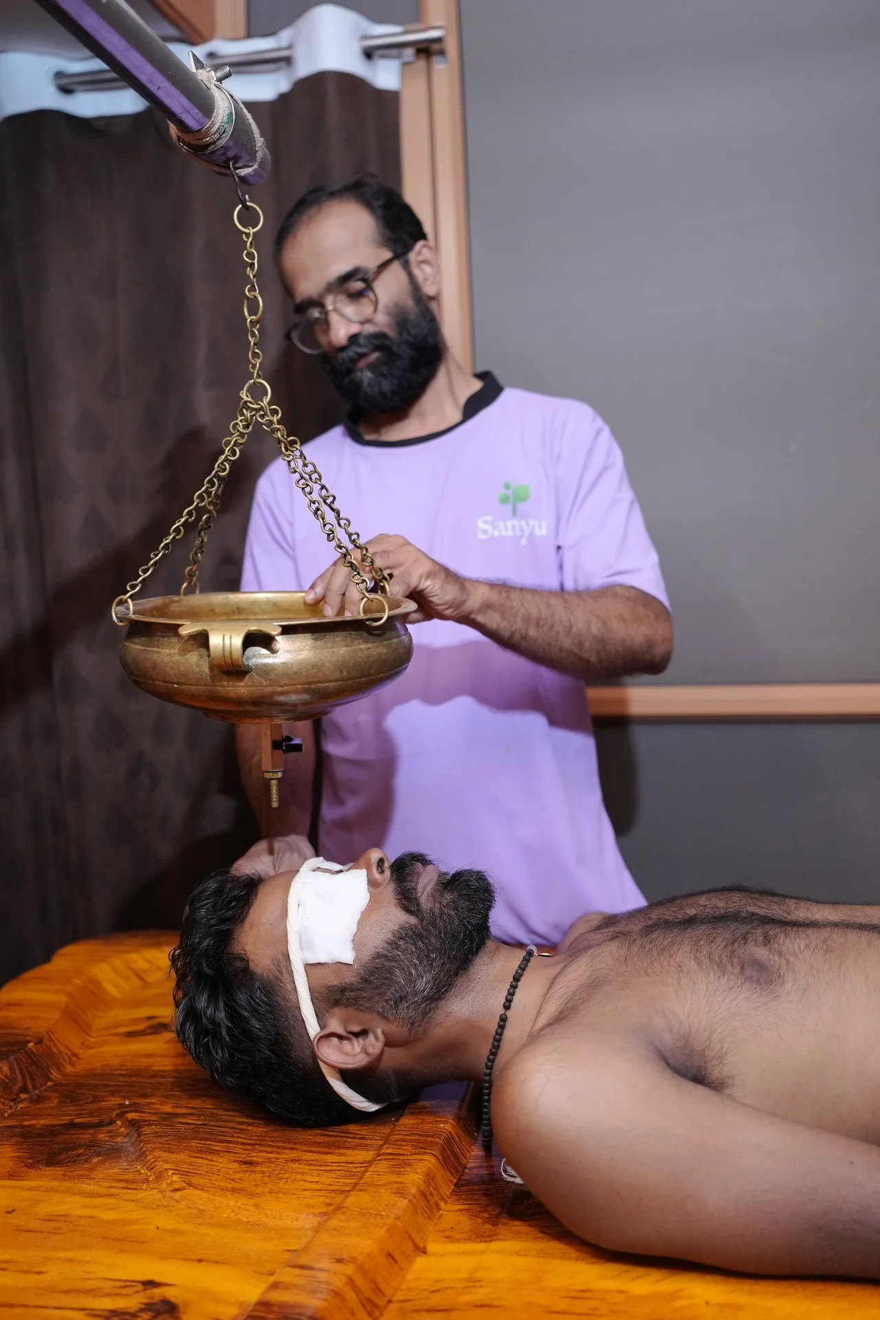 A therapist administering Shirodhara from a traditional brass vessel