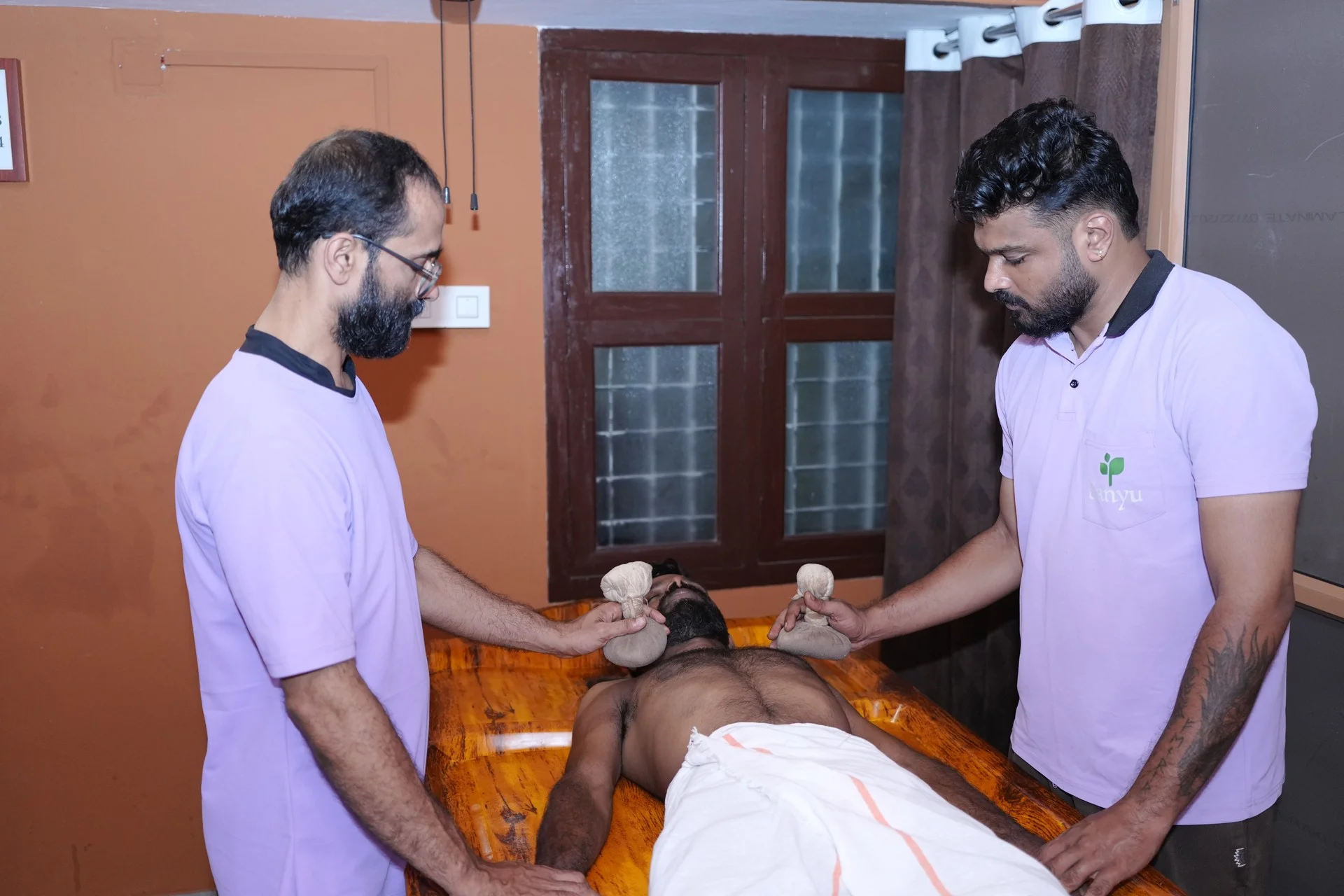 Two Ayurvedic therapists applying warm Kizhi poultices during treatment