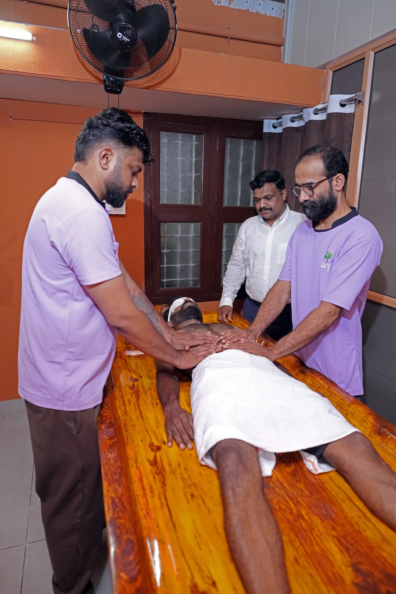 Two Ayurvedic therapists delivering synchronized Abhyanga treatment supervised by Dr. Sudheesh